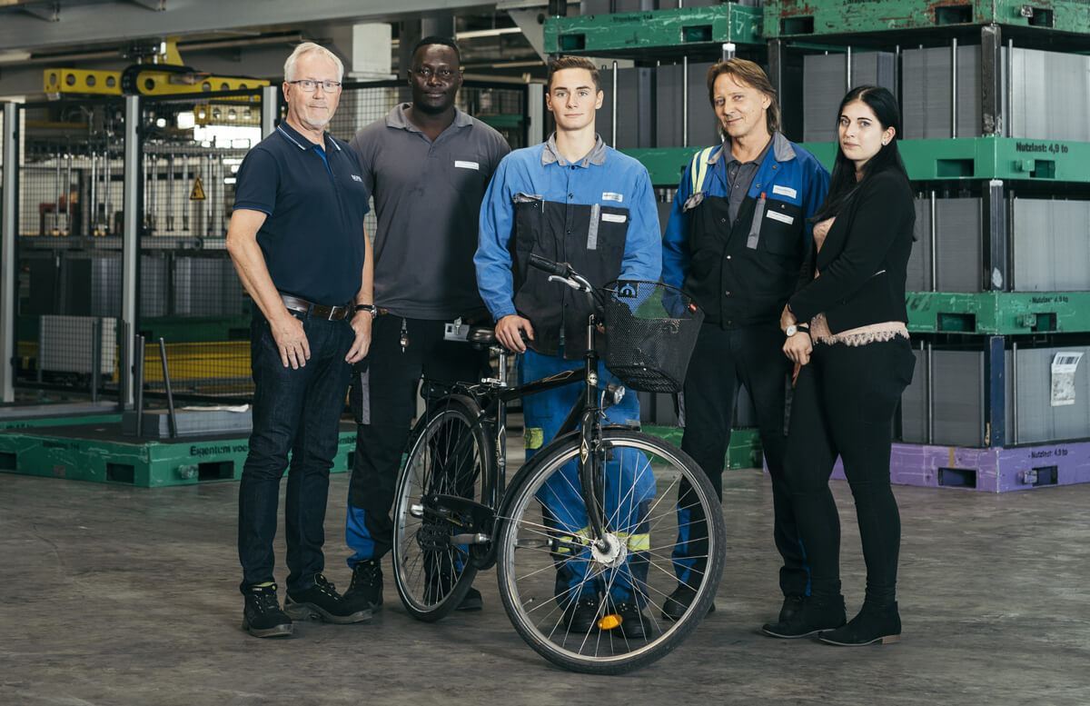 Diverse Gruppe von Mitarbeiterinnen und Mitarbeitern mit posieren einem Fahrrad