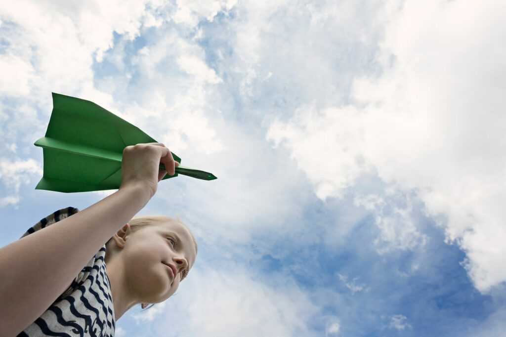 Girl holding a green paper airplane in her right hand