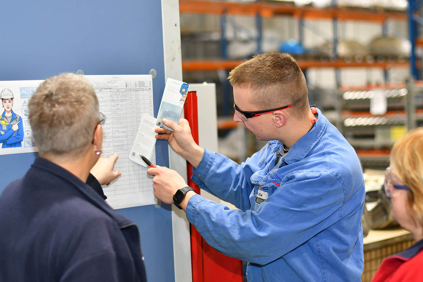 Willi mit zwei Mitarbeitern vor einer Liste zur Organisation an der Wand