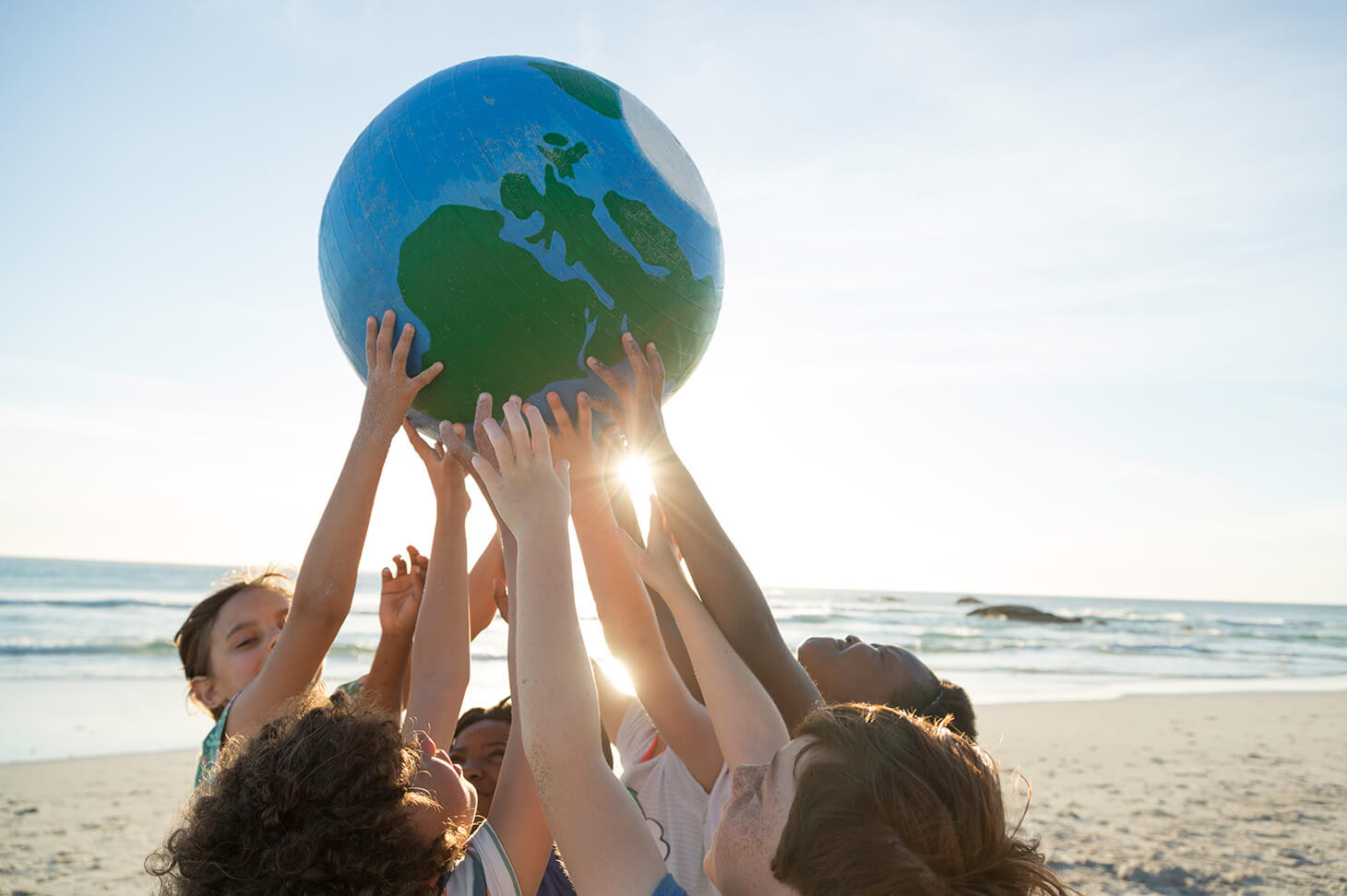 5 children holding a globe together on a sandy beach, the sun shining through their hands