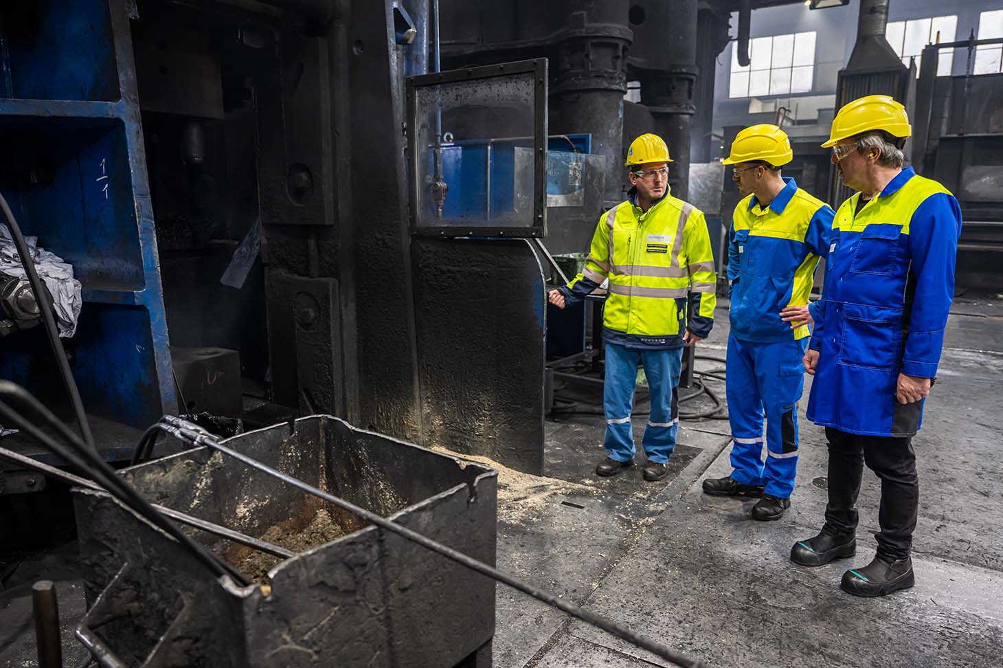 Lothar, Thomas und Sebastian mit Schutzkleidung, Thomas öffnet eine Tür in der Werkshalle