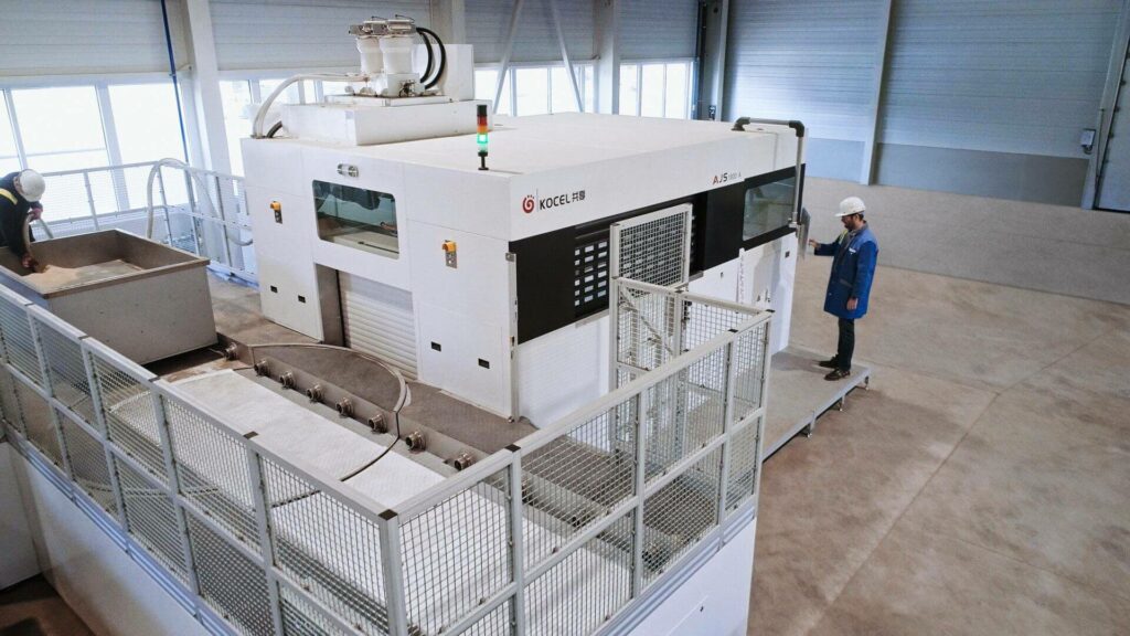 Exterior shot of the 3D sand printer, an employee operates the system from outside on a screen