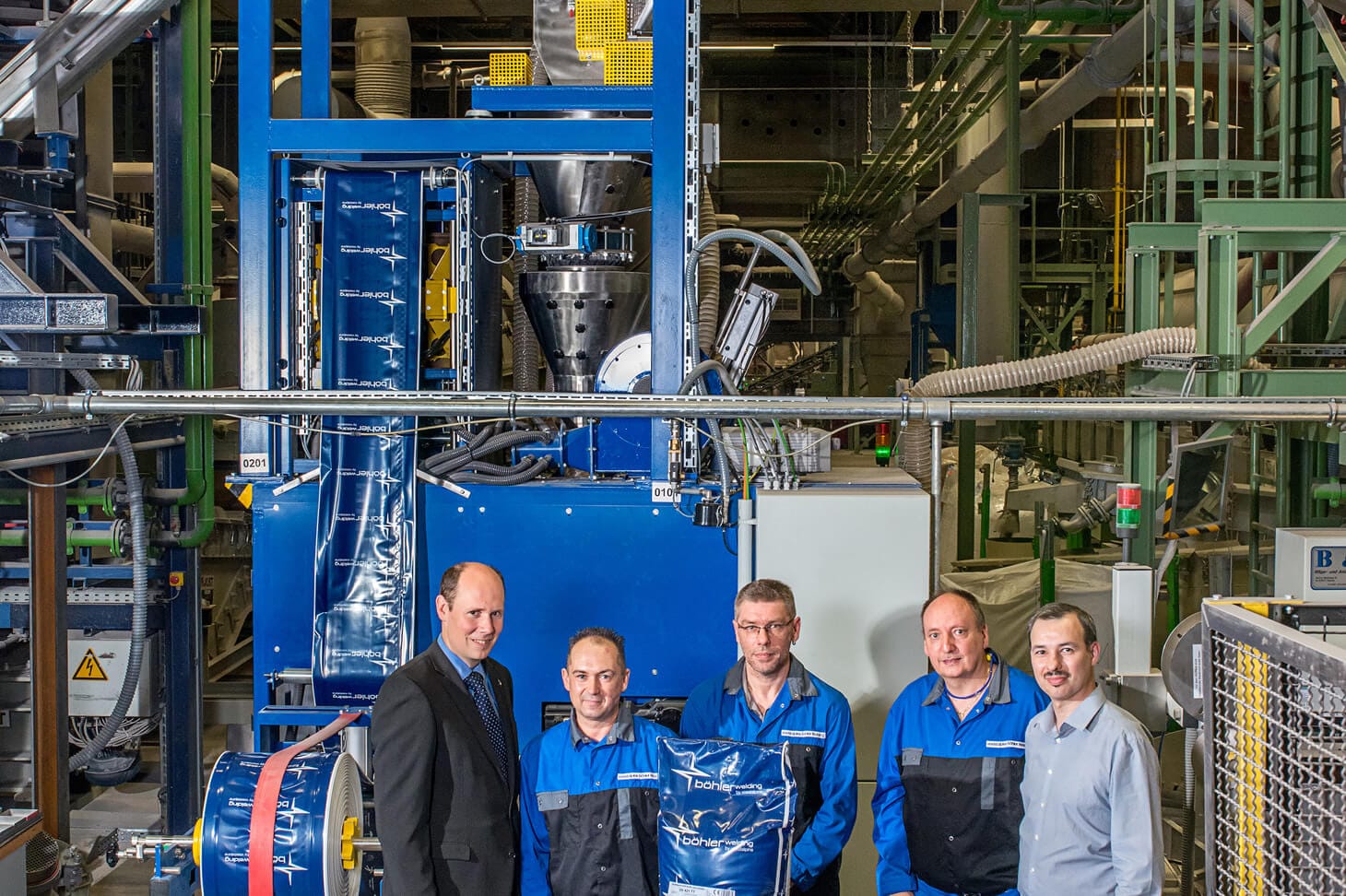 5 Mitarbeiter der voestalpine böhler welding hamm posieren in einer Hallo vor der Vakuum-Absackanlage