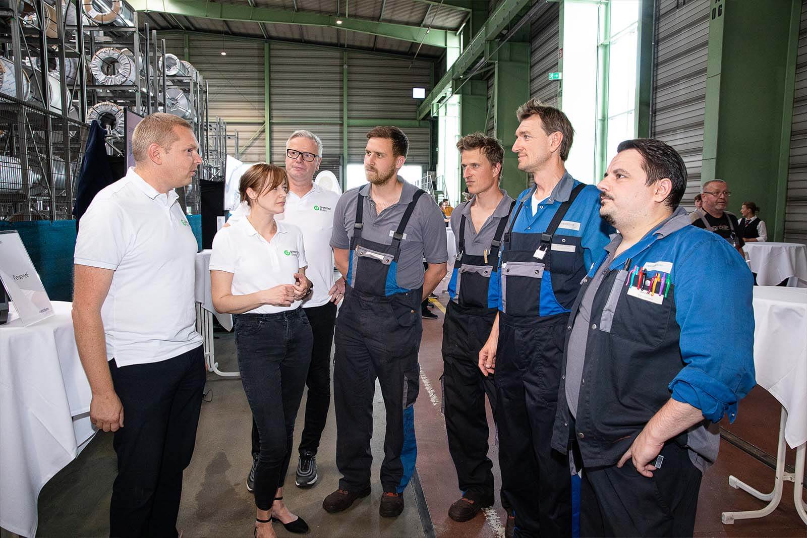 vier voestalpine Mitarbeiter in Arbeitskleidung und eine Mitarbeiterin und zwei Mitarbeiter mit greentec steel shirts