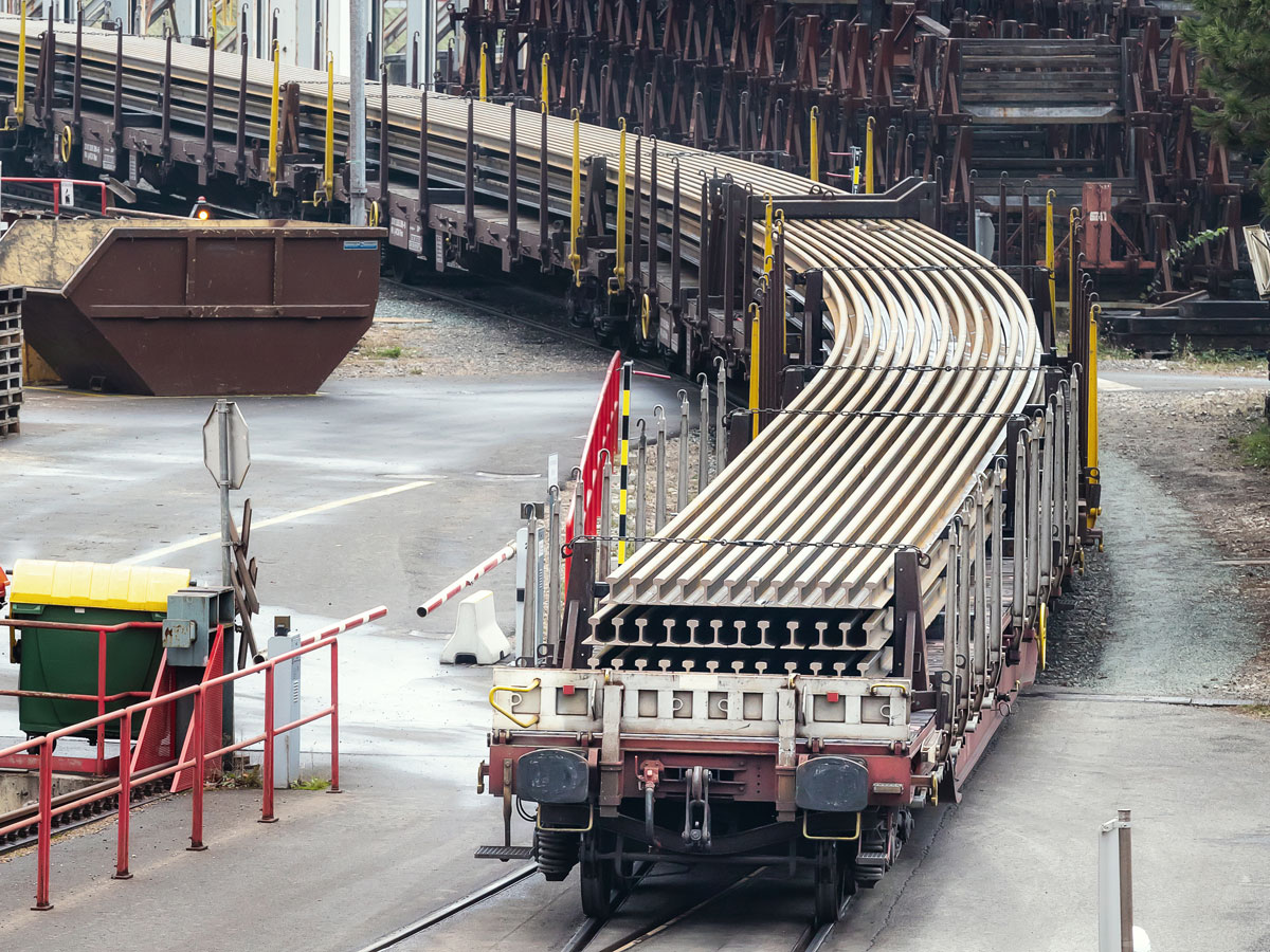 When transporting long rails on train wagons, a curve is negotiated and the transported rails bend through the curve