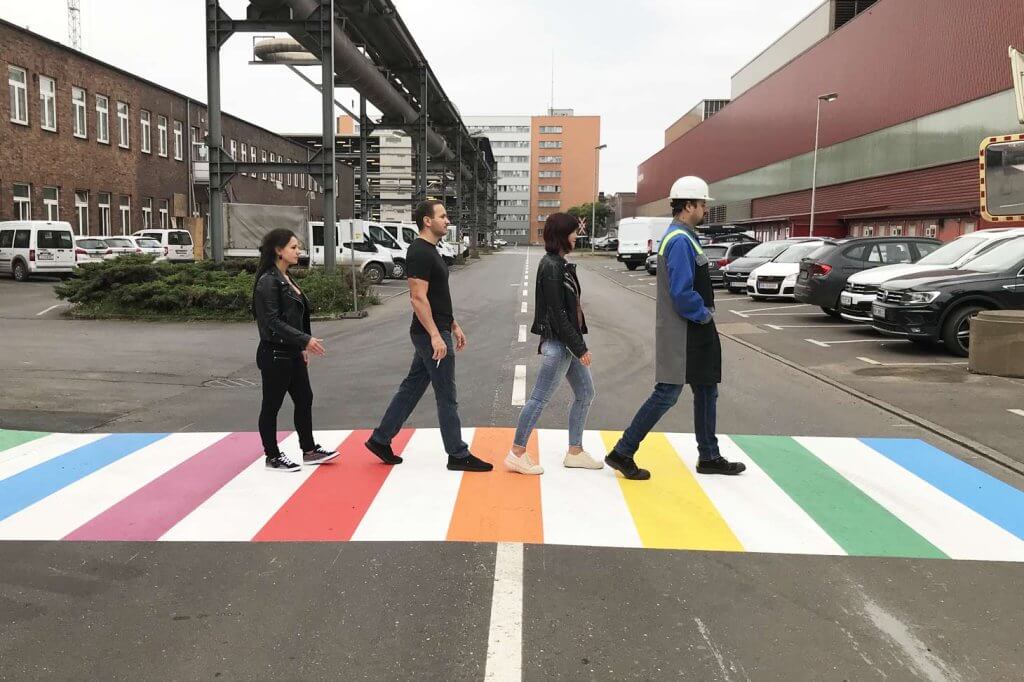 vier Personen gehen über einen regenbogenfarbenen Zebrastreifen am Werksgelände der voestalpine