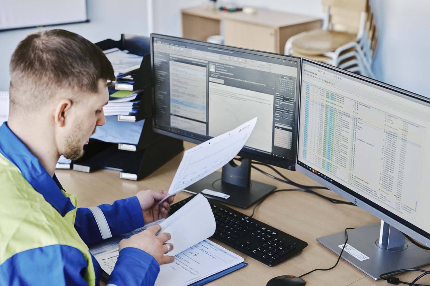 voestalpine Mitarbeiter Thomas bei der Arbeit an seinem Schreibtisch vor zwei Bildschirmen mit einer Mappe