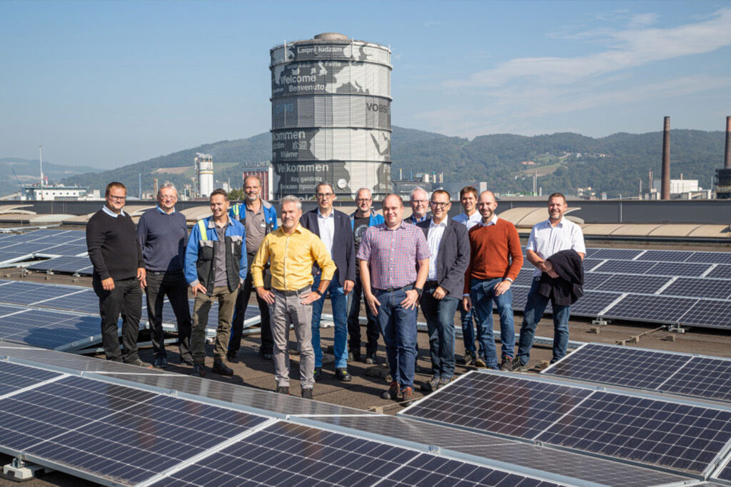 Gruppenfoto zwischen den PV-Paneelen in der voestalpine Linz, im Hintergrund der voestalpine Koksgas Gasometer