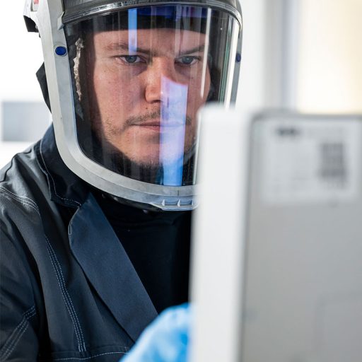 Close-up of Bastian's face wearing a hard hat: he is operating an industrial 3D printer in the Additive Manufacturing Center