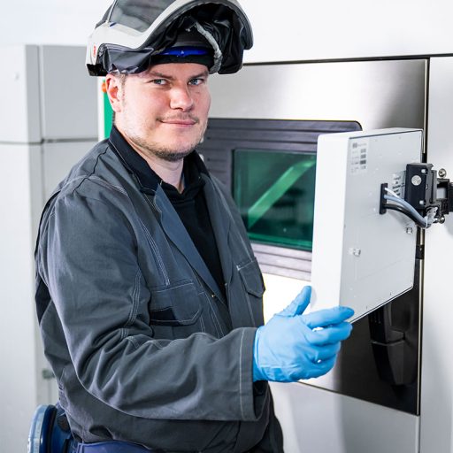 Portrait photo of Bastian operating an industrial 3D printer in the Additive Manufacturing Center