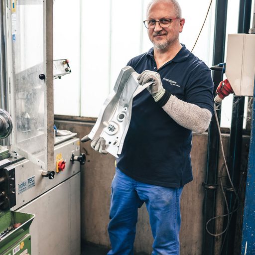 Bernd hält einen Bauteil in seinen Händen, das er aus der Maschine geholt hat