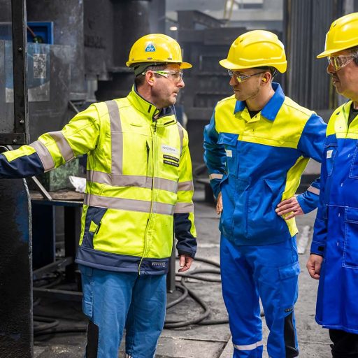 Lothar, Thomas und Sebastian mit Schutzkleidung in der Werkshall, Thomas zeigt nach links