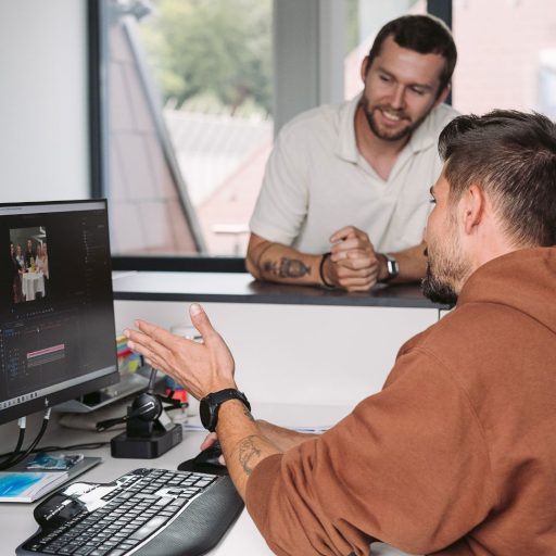 voestalpine Mitarbeiter Michael zeigt seinem Kollegen ein Veranstaltungsfoto am Bildschirm seines Computers