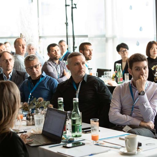 People sit around two rows of tables and follow a presentation on safety at voestalpine.