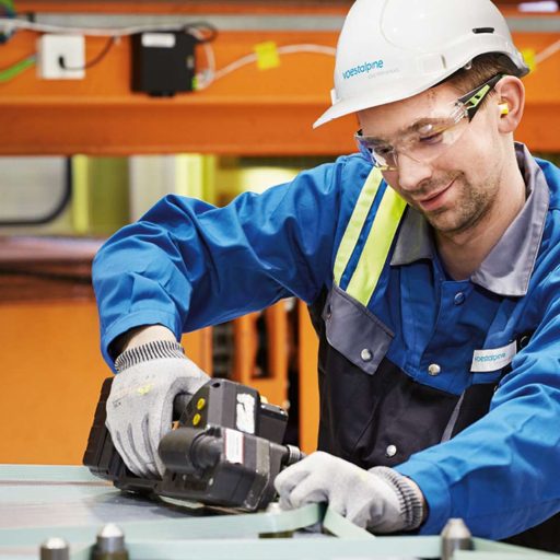 voestalpine employee shows how to work safely with safety helmet, safety goggles and protective gloves