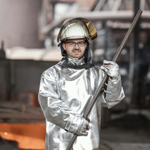 Kevin in HItzeschutzanzug im Portrait vor dem Hochofen