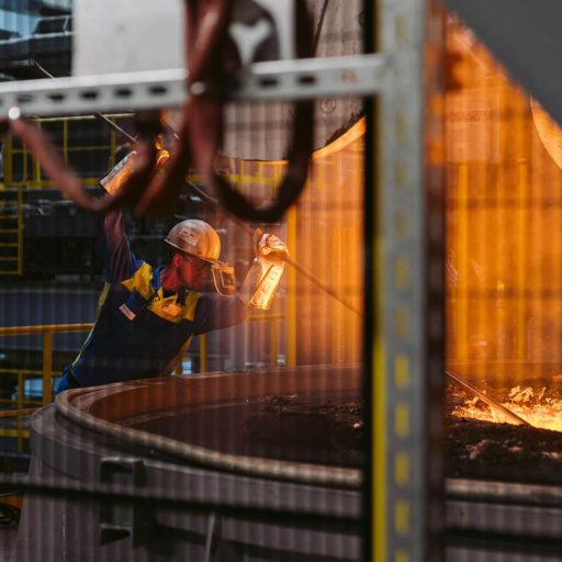 Employee with heat protection suit, visor and gloves holds a steel rod in molten steel