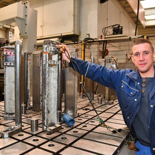 Christian holds his hand on a part in the production hall for automotive components